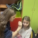 Starsza uczennica maluje farbkami wzór na twarzy młodszej dziewczynki podczas szkolnych andrzejek.