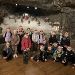 Grupa dzieci pozuje na tle solnej szopki z figurami przedstawiającymi scenę Bożego Narodzenia.