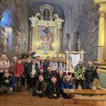 Dzieci stoją przed solnym ołtarzem w kaplicy podziemnej, otoczone rzeźbami i elementami ozdobnymi wykutymi w skale