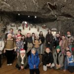 Grupa dzieci pozuje na tle solnej szopki z figurami przedstawiającymi scenę Bożego Narodzenia.”