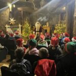 Grupa uczniów słucha Świętego Mikołaja przemawiającego w podziemnej komorze, wśród choinek i dekoracji świątecznych