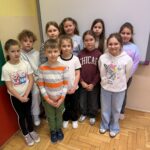 Grupa uczniów szkoły podstawowej stoi w sali lekcyjnej, ustawiona w dwóch rzędach. Dzieci pozują do wspólnego zdjęcia, ubrane w codzienne stroje. Wśród nich znajdują się laureatki konkursu ekologicznego.