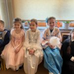 Uczniowie klas I–III w strojach karnawałowych siedzą na ławce w sali szkolnej podczas zabawy karnawałowej.