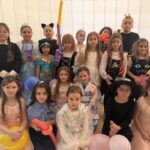 Grupa uczniów klas I–III w przebraniach karnawałowych pozuje do wspólnego zdjęcia w sali szkolnej podczas zabawy karnawałowej.