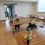 Uczniowie siedzą przy stołach podczas etapu gminnego Ogólnopolskiego Turnieju Wiedzy Pożarniczej. Na stołach stoją butelki z napojami i szklanki, a uczestnicy przygotowują się do konkursu w jasnej sali.