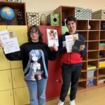 Dwoje uczniów stoi w szkolnej sali przed kolorowymi szafkami i trzyma dyplomy oraz nagrody zdobyte w szkolnym etapie konkursu „Góralskie Cytanie”. W tle widoczne są półki z pomocami dydaktycznymi.