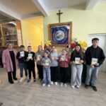 grupa nagrodzonych uczniów prezentuje dyplomy i upominki na tle wiosennej wystawy pisanek i dekoracji wielkanocnych.