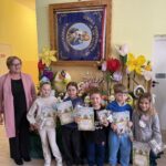 grupa nagrodzonych uczniów prezentuje dyplomy i upominki na tle wiosennej wystawy pisanek i dekoracji wielkanocnych.