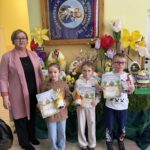 grupa nagrodzonych uczniów prezentuje dyplomy i upominki na tle wiosennej wystawy pisanek i dekoracji wielkanocnych.