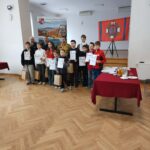 Uczestnicy konkursu stoją w grupie z dyplomami i nagrodami po zakończeniu etapu gminnego Ogólnopolskiego Turnieju Wiedzy Pożarniczej. Za nimi widoczny jest baner gminy oraz flaga strażacka.