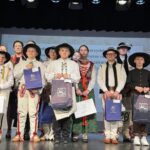 Uczniowie w tradycyjnych strojach góralskich stoją na scenie z torbami nagrodowymi podczas uroczystego wręczenia nagród.