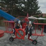 Dwie dziewczynki siedzą w czerwonym samolocie będącym atrakcją lunaparku w Zatorlandzie.