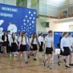 Uczniowie prezentują układ taneczny podczas części artystycznej uroczystości. W tle znajduje się dekoracja przedstawiająca zegar, motyle, pióro i napis Czas rozwinąć skrzydła